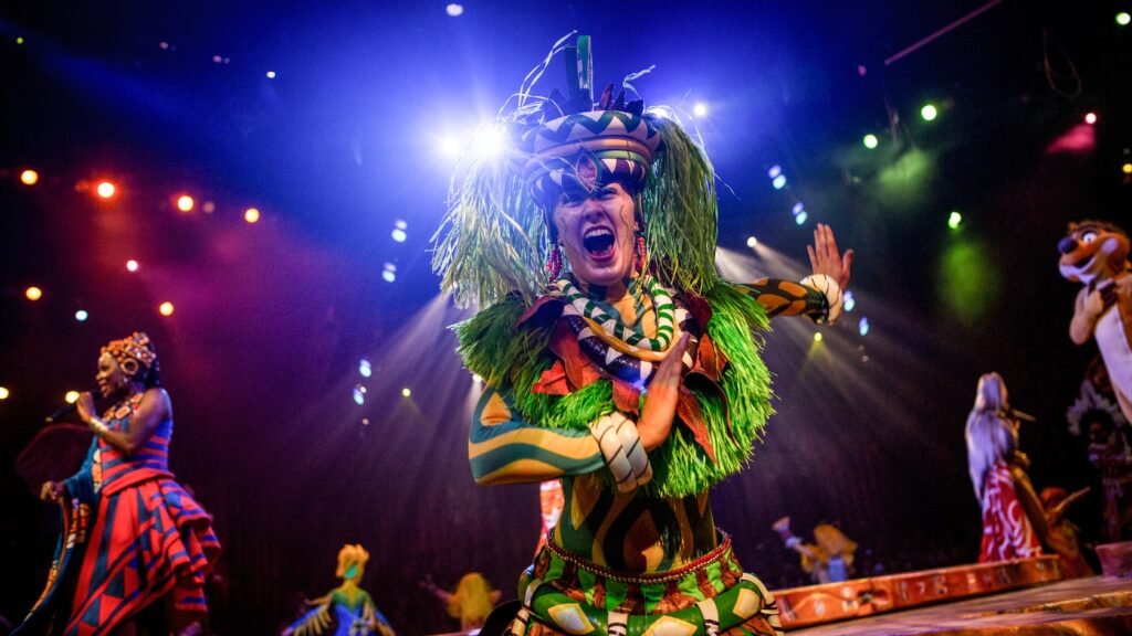 A smiling performer in a colorful outfit with long blades of grass in her headpiece