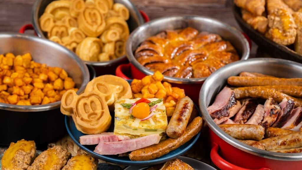 A breakfast buffet spread with Mickey shaped waffles, sausages, ham, pastries and roasted potatoes