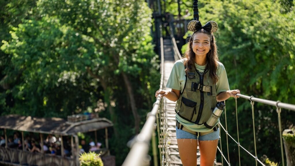 A girl wearing Mickey ears and a vest stands on a rope bridge at Disney's Animal Kingdom theme park