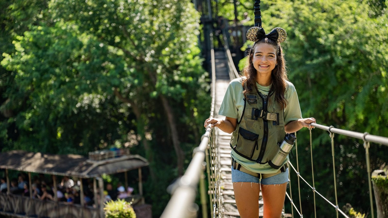 A girl wearing Mickey ears and a vest stands on a rope bridge at Disney's Animal Kingdom theme park